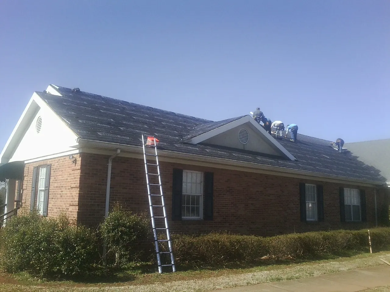 Crew tearing shingles off a brick ranch roof with a ladder set — Metal Roof Repair work by our crew in Irvine