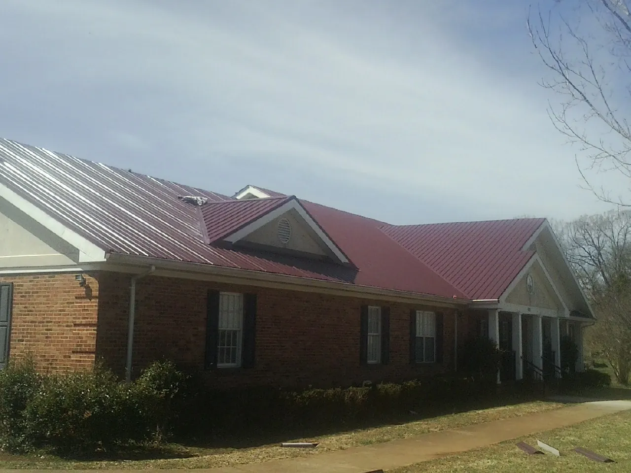 Red metal roof with gabled entries on a long brick building, from a Hail Damage Roof Repair job in Irvine