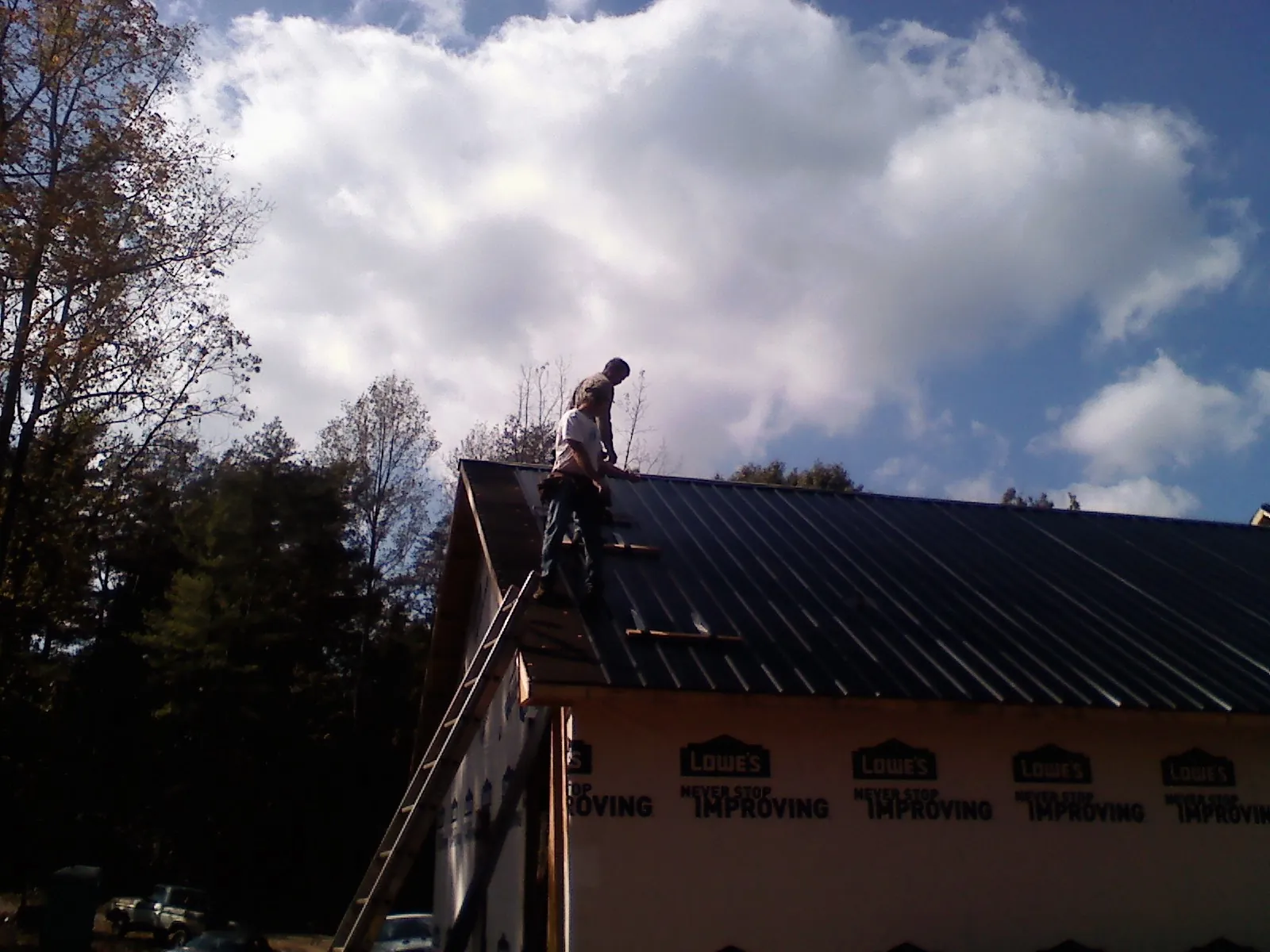 Roofer fastening dark metal panels high against a cloudy sky, from a Roof Inspection job in Irvine